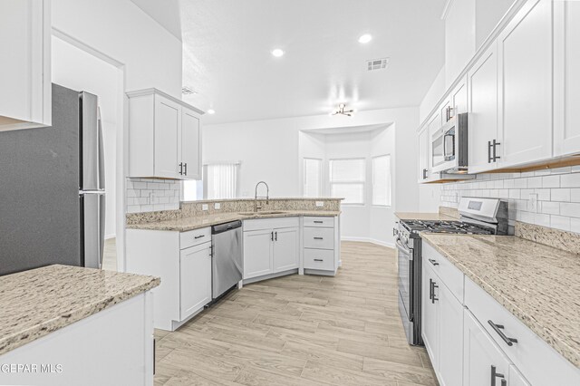 kitchen with a sink, stainless steel appliances, a peninsula, backsplash, and visible vents