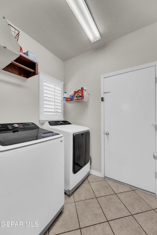laundry area with washing machine and clothes dryer, a textured ceiling, laundry area, and light tile patterned floors
