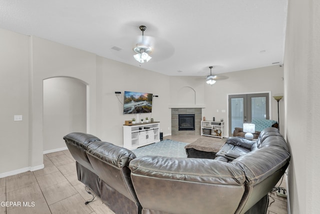 living area featuring arched walkways, a ceiling fan, baseboards, a tile fireplace, and visible vents