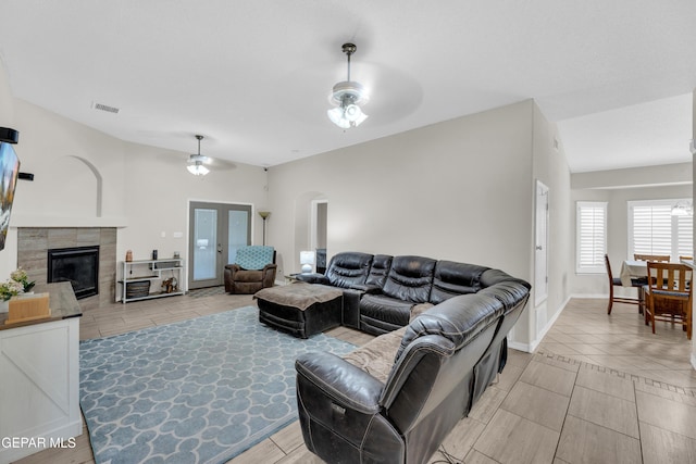 living area with visible vents, arched walkways, a tiled fireplace, a ceiling fan, and light tile patterned floors