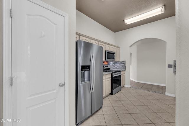 kitchen with arched walkways, tasteful backsplash, light tile patterned floors, baseboards, and stainless steel appliances