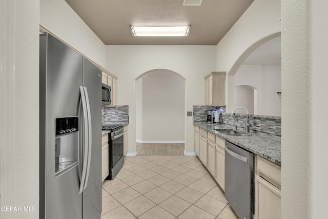kitchen with decorative backsplash, appliances with stainless steel finishes, a sink, light stone counters, and light tile patterned flooring