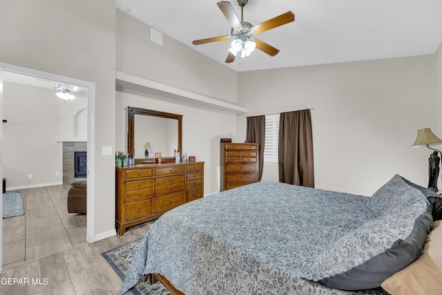 bedroom with a ceiling fan, visible vents, vaulted ceiling, a tile fireplace, and baseboards