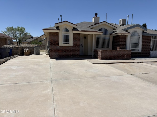 view of front of house with a gate, central AC unit, a chimney, and brick siding