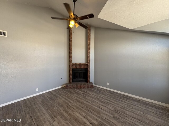 unfurnished living room featuring dark wood-style flooring, ceiling fan, a brick fireplace, baseboards, and vaulted ceiling