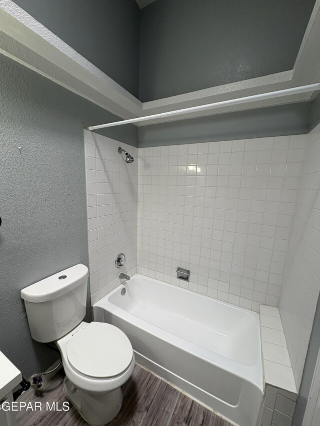 bathroom with tub / shower combination, a textured wall, wood finished floors, and toilet