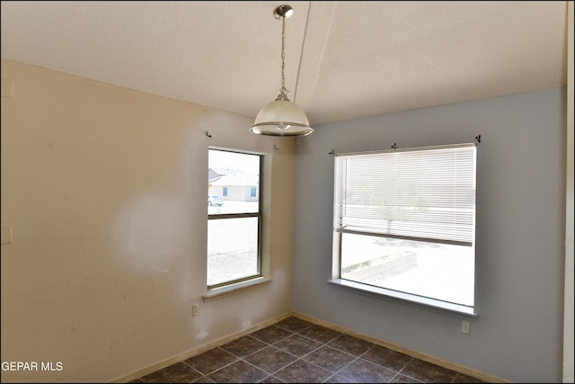 unfurnished dining area with baseboards, a textured ceiling, and dark tile patterned flooring