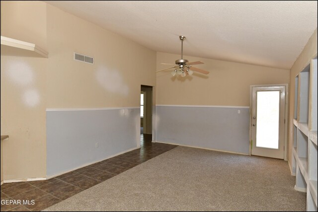empty room with a ceiling fan, visible vents, vaulted ceiling, dark tile patterned flooring, and dark colored carpet