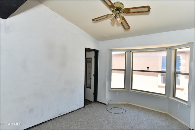 carpeted empty room featuring a ceiling fan, baseboards, vaulted ceiling, and plenty of natural light