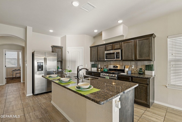1021 Aerodyne Pl, El Paso, TX 79928 - kitchen with appliances with stainless steel finishes, a sink, arched walkways, dark brown cabinetry, and a kitchen island with sink