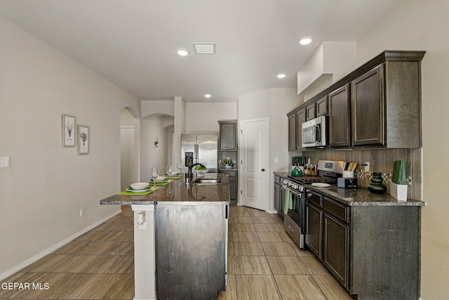 1021 Aerodyne Pl, El Paso, TX 79928 - kitchen featuring stainless steel appliances, arched walkways, dark brown cabinetry, an island with sink, and a sink