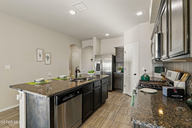 1021 Aerodyne Pl, El Paso, TX 79928 - kitchen with stainless steel appliances, a sink, arched walkways, a kitchen island with sink, and dark stone countertops