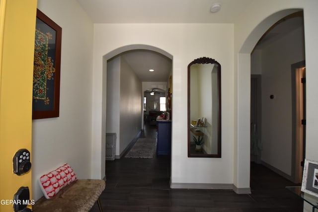 hall featuring dark wood-type flooring, arched walkways, and baseboards