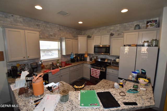 kitchen featuring visible vents, light stone countertops, tasteful backsplash, a sink, and stainless steel appliances