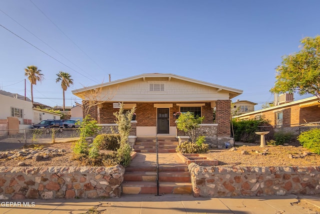 bungalow-style home featuring a porch, brick siding, and fence