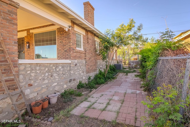 view of side of property with brick siding, central AC, fence, and a chimney