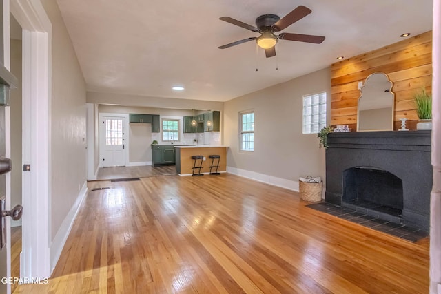 unfurnished living room featuring a ceiling fan, baseboards, recessed lighting, a fireplace with flush hearth, and light wood-style flooring