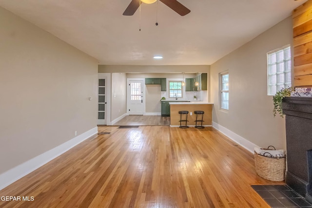 living area featuring baseboards, ceiling fan, and light wood finished floors
