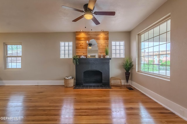 unfurnished living room featuring a fireplace with flush hearth, baseboards, a ceiling fan, and wood finished floors