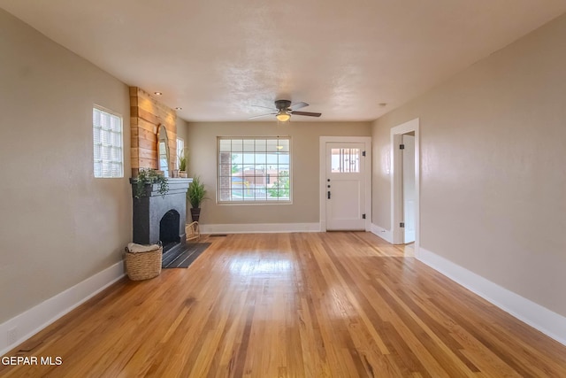 unfurnished living room with baseboards, a ceiling fan, light wood-style floors, and a large fireplace