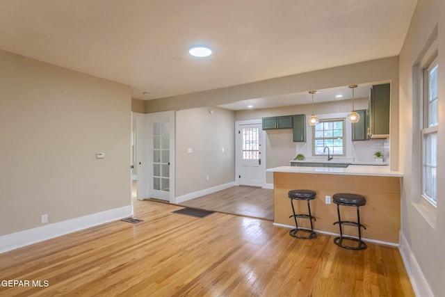 kitchen with a breakfast bar area, a peninsula, green cabinetry, and light wood-style flooring
