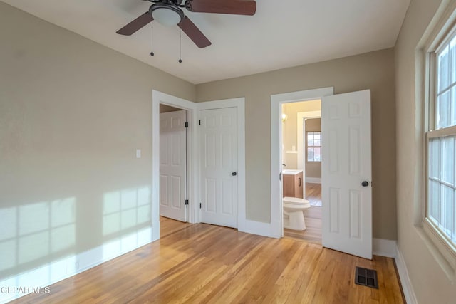 unfurnished bedroom featuring ensuite bath, light wood-style flooring, a ceiling fan, baseboards, and visible vents