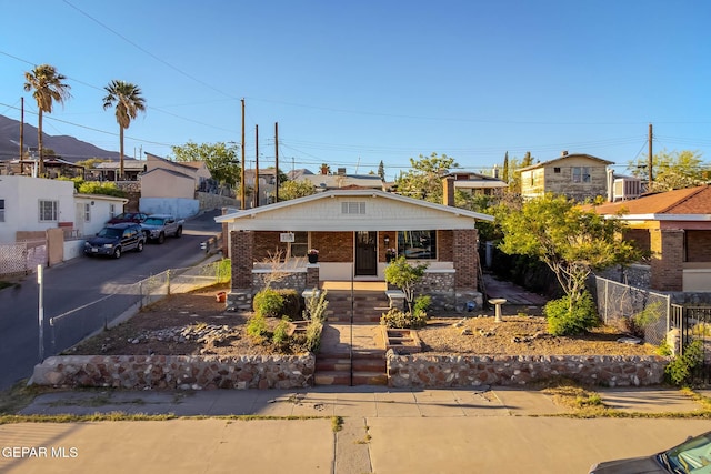 bungalow featuring a porch, brick siding, and fence