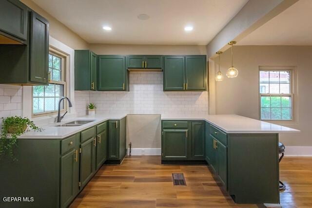 kitchen with a peninsula, light wood-type flooring, a sink, and green cabinets