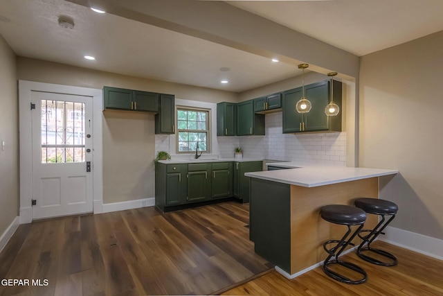 kitchen featuring dark wood-style flooring, a sink, baseboards, green cabinets, and a peninsula
