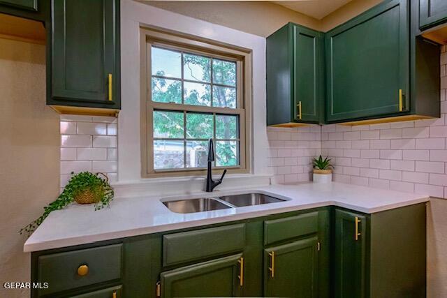 kitchen featuring light countertops, backsplash, a sink, and green cabinets