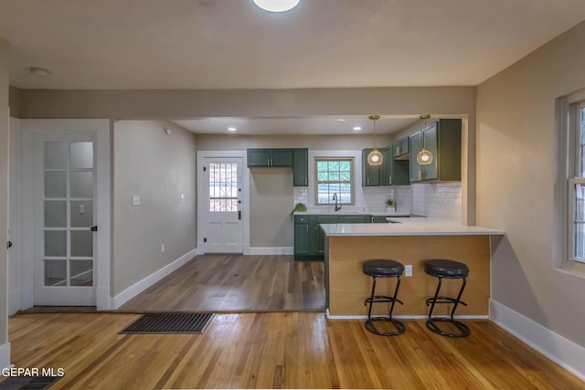 kitchen with a peninsula, baseboards, wood finished floors, backsplash, and green cabinets