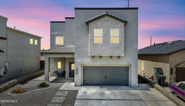 view of front of house featuring a tile roof, stone siding, a garage, stucco siding, and driveway