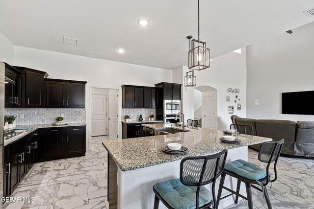 kitchen featuring marble finish floor, light stone countertops, an island with sink, stainless steel microwave, and arched walkways