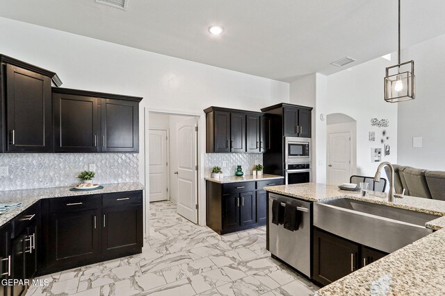 kitchen with appliances with stainless steel finishes, arched walkways, a sink, light stone counters, and marble finish floor