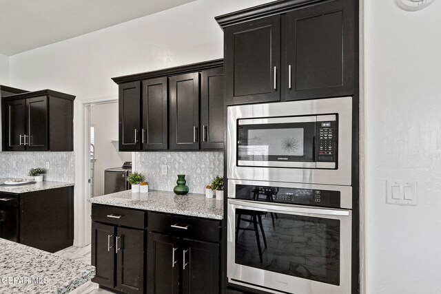 kitchen with appliances with stainless steel finishes, decorative backsplash, light stone countertops, and dark cabinetry