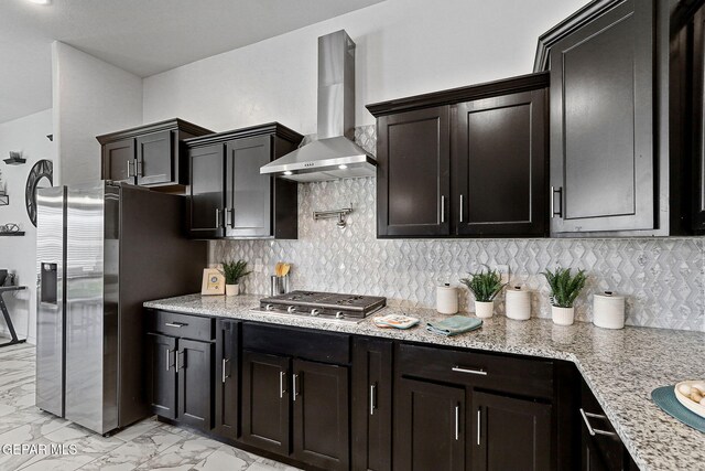 kitchen with marble finish floor, light stone countertops, wall chimney exhaust hood, tasteful backsplash, and appliances with stainless steel finishes