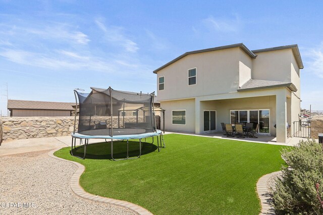 back of house featuring a lawn, a patio area, a trampoline, and stucco siding