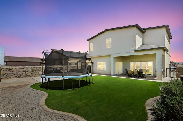 rear view of property with a patio, a trampoline, stucco siding, and a yard