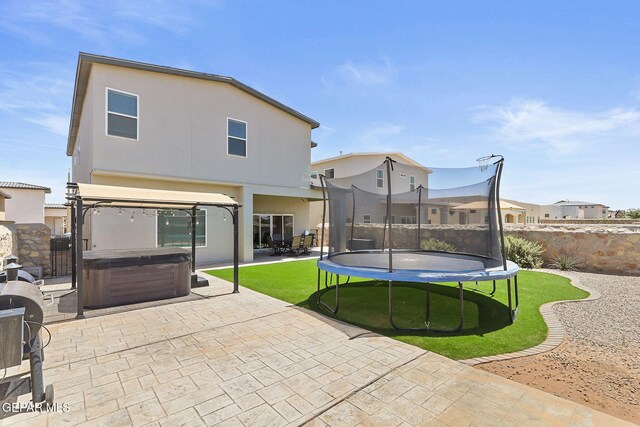rear view of house with a trampoline, a hot tub, a yard, a patio, and stucco siding