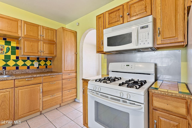 kitchen with brown cabinetry, light tile patterned flooring, white appliances, tasteful backsplash, and arched walkways