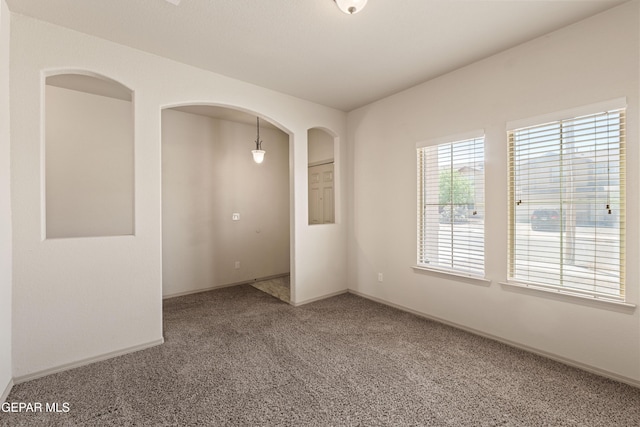 carpeted empty room with baseboards and arched walkways