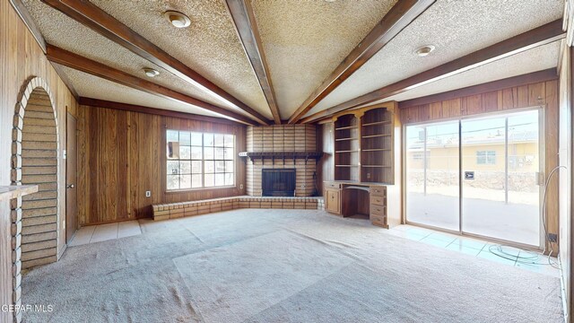 6001 Canton Ct, El Paso, TX 79905 - unfurnished living room with a textured ceiling, a brick fireplace, beamed ceiling, wooden walls, and carpet