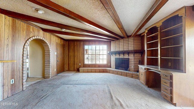 6001 Canton Ct, El Paso, TX 79905 - unfurnished living room with light colored carpet, wood walls, a brick fireplace, and beam ceiling