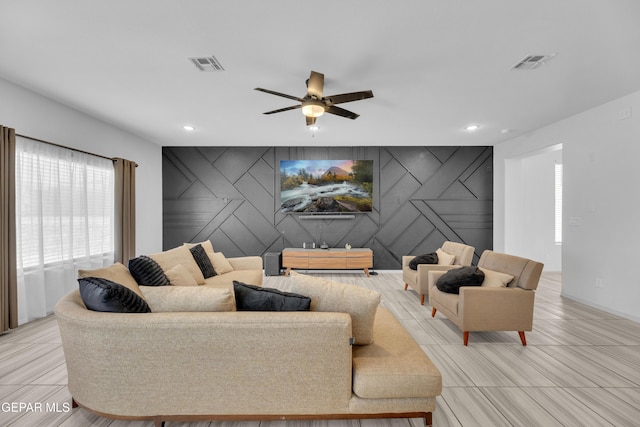 living room featuring ceiling fan, visible vents, and an accent wall