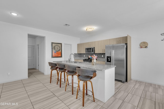 kitchen featuring decorative backsplash, visible vents, appliances with stainless steel finishes, a sink, and a breakfast bar