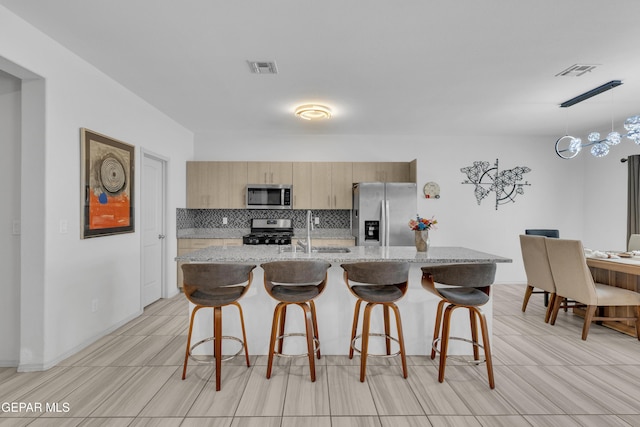 kitchen featuring visible vents, a breakfast bar, tasteful backsplash, a sink, and appliances with stainless steel finishes