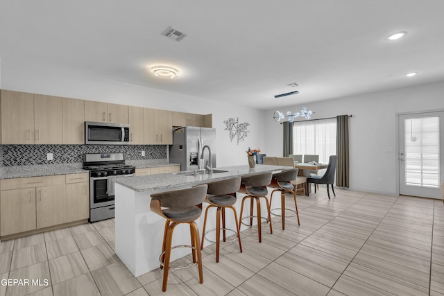 kitchen with a kitchen breakfast bar, decorative backsplash, light brown cabinetry, a sink, and stainless steel appliances