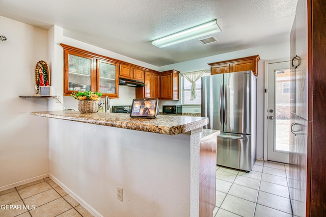 14253 Hacienda Rock Dr, El Paso, TX 79938 - kitchen featuring freestanding refrigerator, under cabinet range hood, a peninsula, light tile patterned flooring, and brown cabinetry
