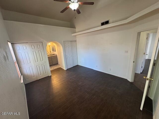 unfurnished bedroom featuring visible vents, lofted ceiling, two closets, dark wood-style floors, and arched walkways