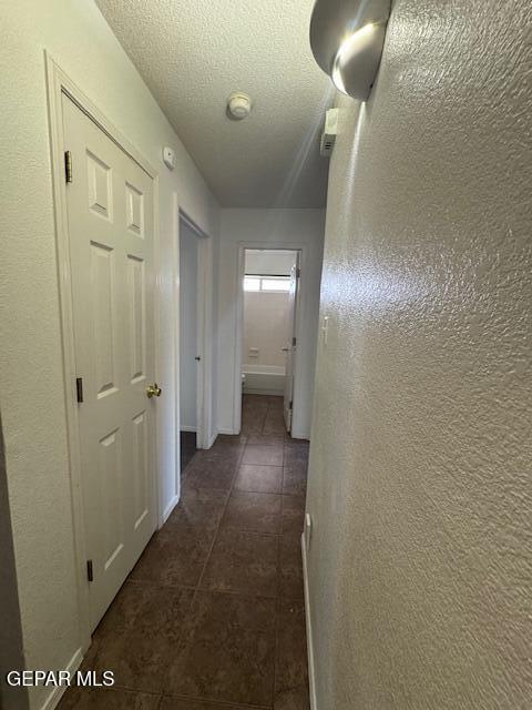 hall with a textured ceiling, a textured wall, and dark tile patterned flooring
